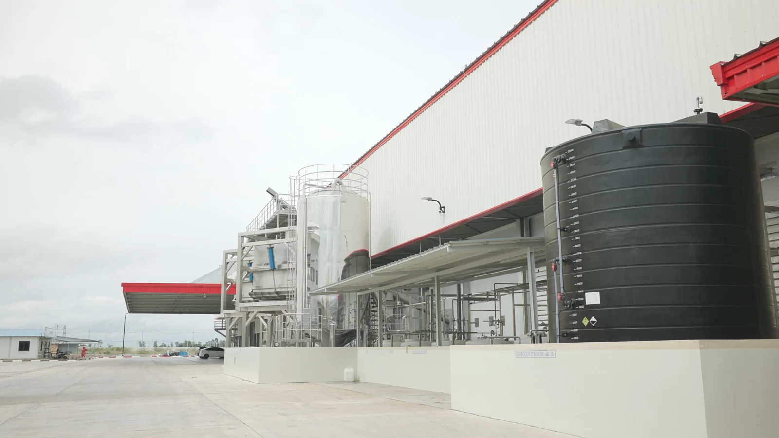 Factory building exterior with tanks and pipework beside the access road